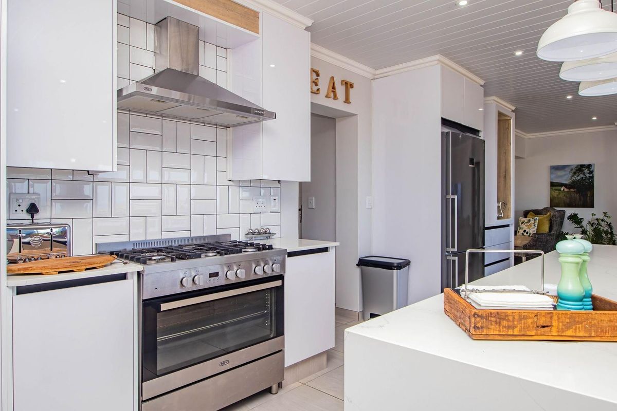 Modern kitchen featuring white cabinetry, subway tile backsplash, stainless steel gas stove with extractor fan, and a large central island with stone countertop.