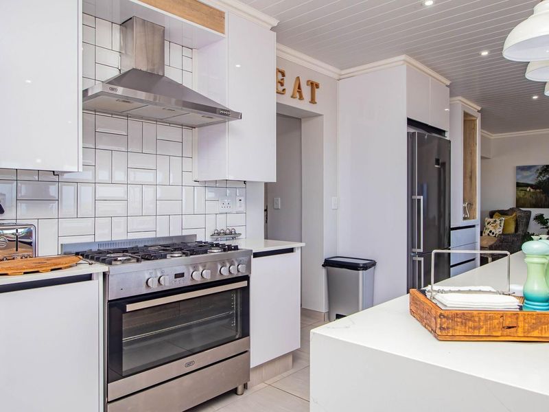 Modern kitchen featuring white cabinetry, subway tile backsplash, stainless steel gas stove with extractor fan, and a large central island with stone countertop.