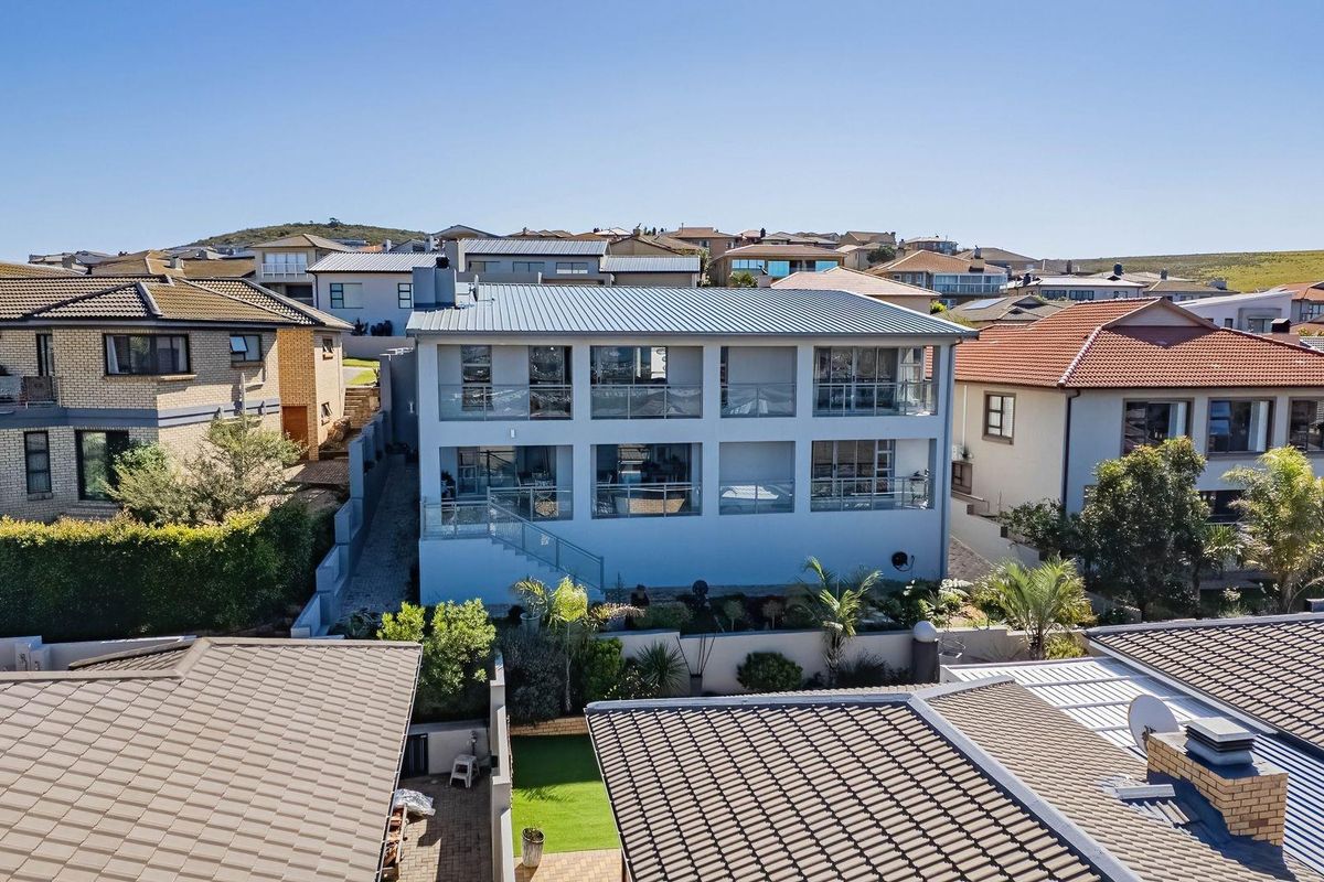 Aerial view of a modern multi-story residential property featuring expansive glass balconies, a metal roof, and a landscaped rear garden area.