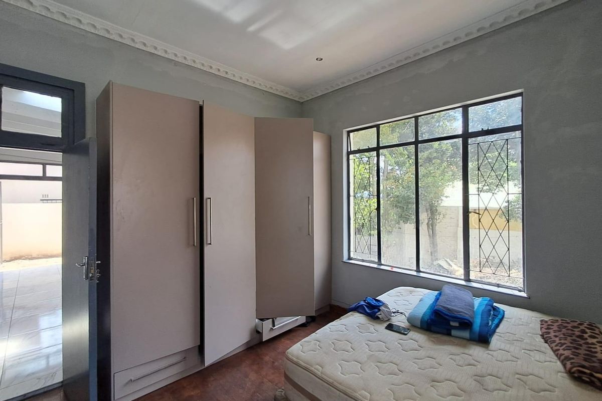 A bedroom featuring built-in wardrobes, large windows with security bars, and crown molding detail.