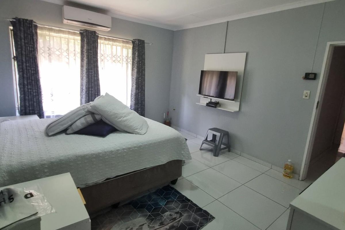 A bedroom featuring tiled flooring, a wall-mounted television unit, and a split-system air conditioner.