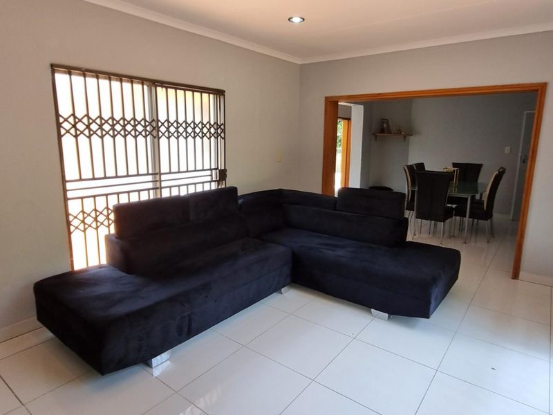 A living room featuring tiled flooring, recessed downlights, and security gates on the sliding door, with an open transition to the dining area.