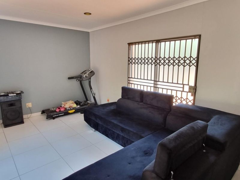 A living room featuring tiled flooring, an air conditioning unit, and a security gate over the window.
