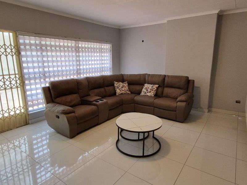 A well-maintained living room featuring polished floor tiles, a sliding door with a security gate, and modern roller blinds.