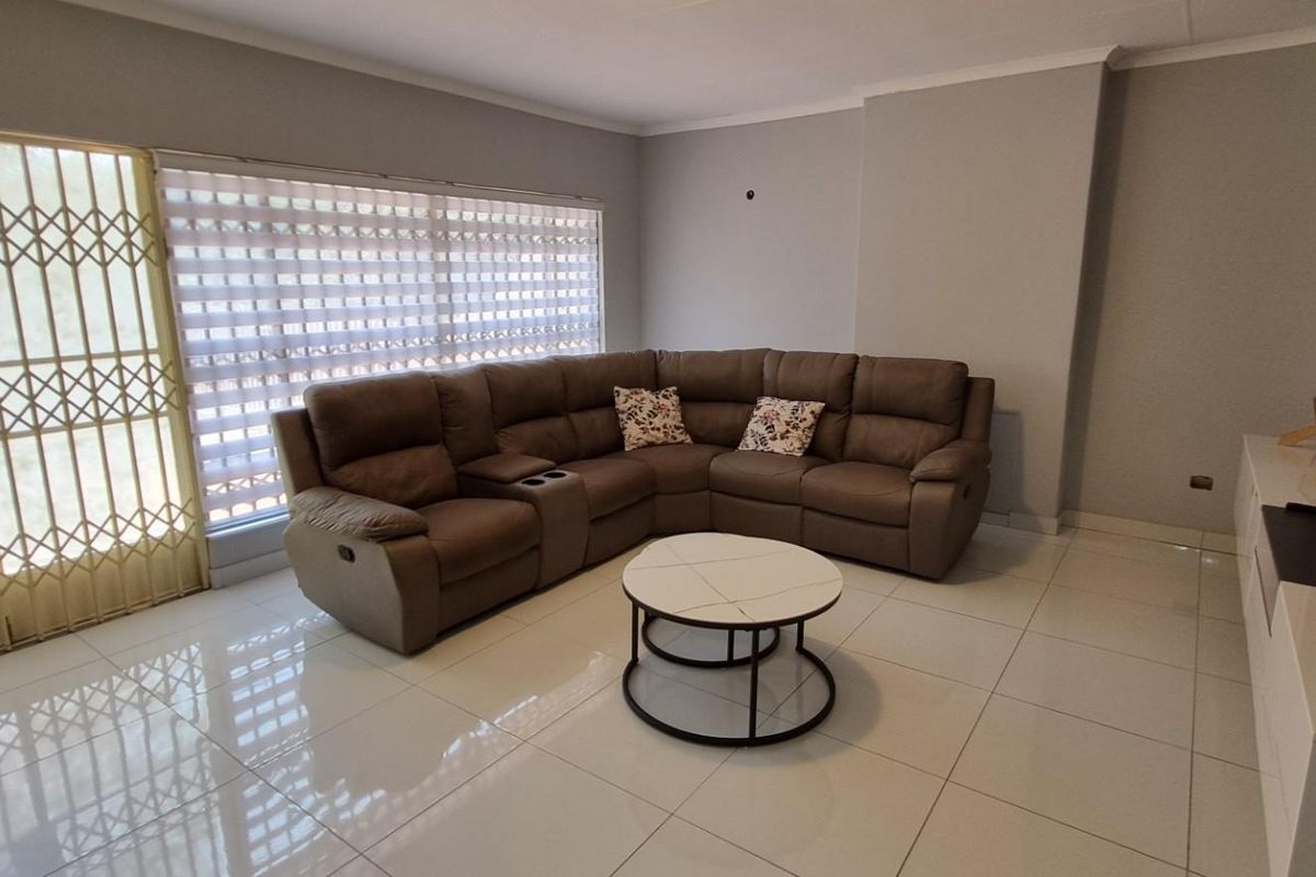 A well-maintained living room featuring polished floor tiles, a sliding door with a security gate, and modern roller blinds.