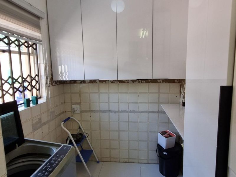 Laundry area featuring white built-in cabinetry, tiled splashback, and a security gate on the window. Requires finishing touches to wall surfaces.