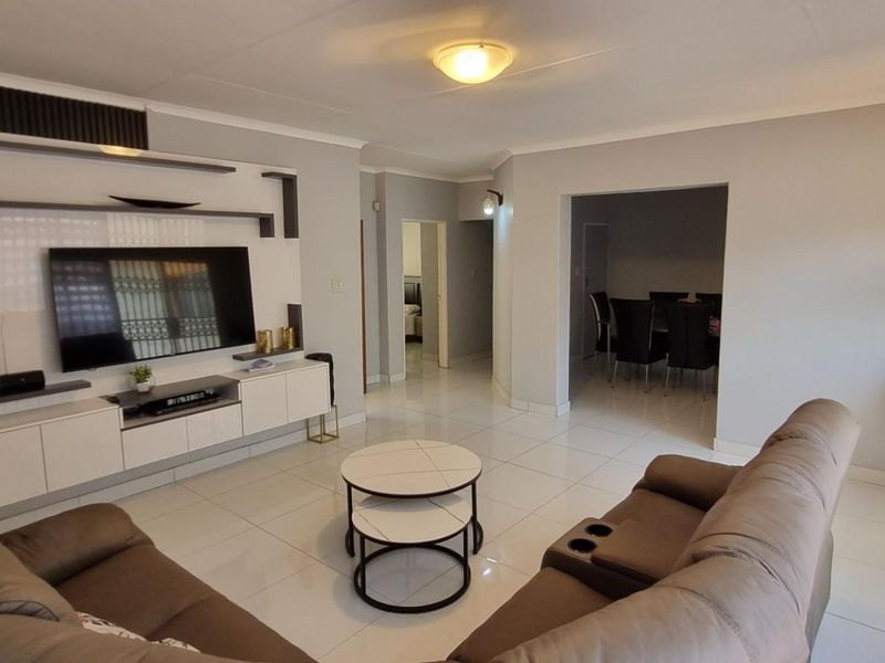 Spacious living room featuring modern tiled flooring, a sleek built-in media wall unit, and neutral finishes, with an open flow to the dining area.