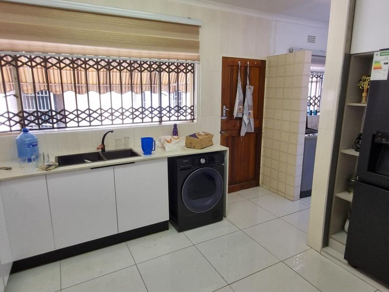 A functional kitchen featuring white cabinetry, dark countertops, a double sink, induction hob, and tiled flooring with a security gate on the window.