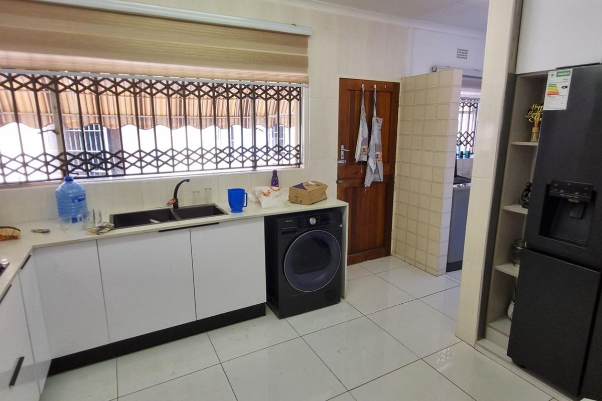 A functional kitchen featuring white cabinetry, dark countertops, a double sink, induction hob, and tiled flooring with a security gate on the window.