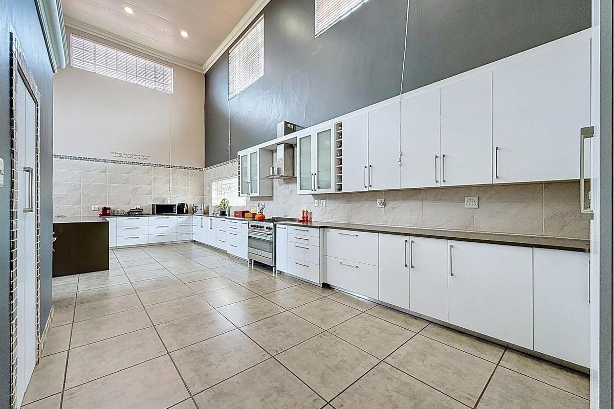 Spacious kitchen featuring high ceilings, extensive white cabinetry, tiled flooring, and a built-in stainless steel oven and extractor fan.