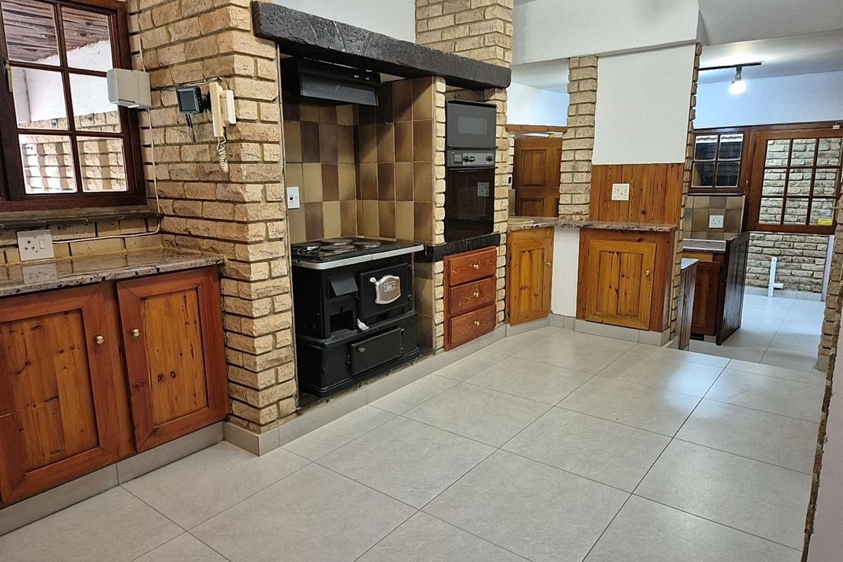 A rustic kitchen featuring exposed brick pillars, timber cabinetry, a built-in stove, and tiled flooring, offering a traditional and functional cooking space.