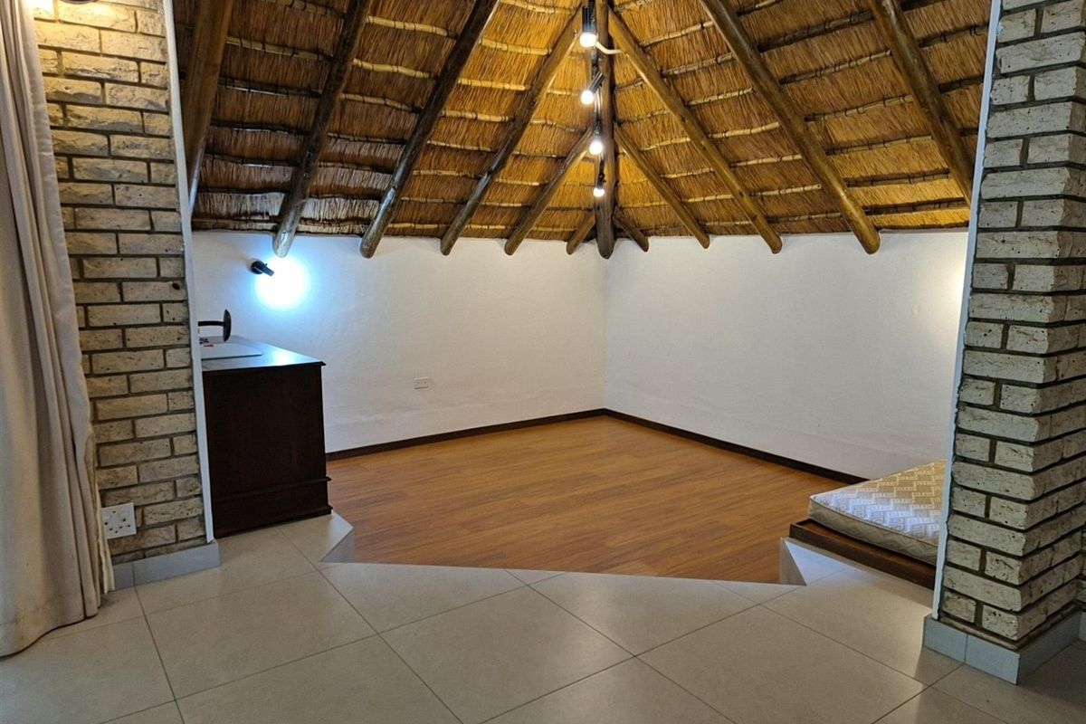 A unique loft-style bedroom featuring a high thatched roof, exposed brick pillars, and a split-level floor design with laminate and tiled flooring.