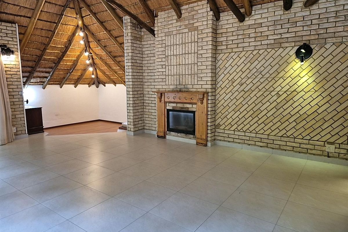 Spacious living area featuring a high vaulted thatched ceiling, exposed timber beams, and a prominent brick fireplace with a wooden mantelpiece.