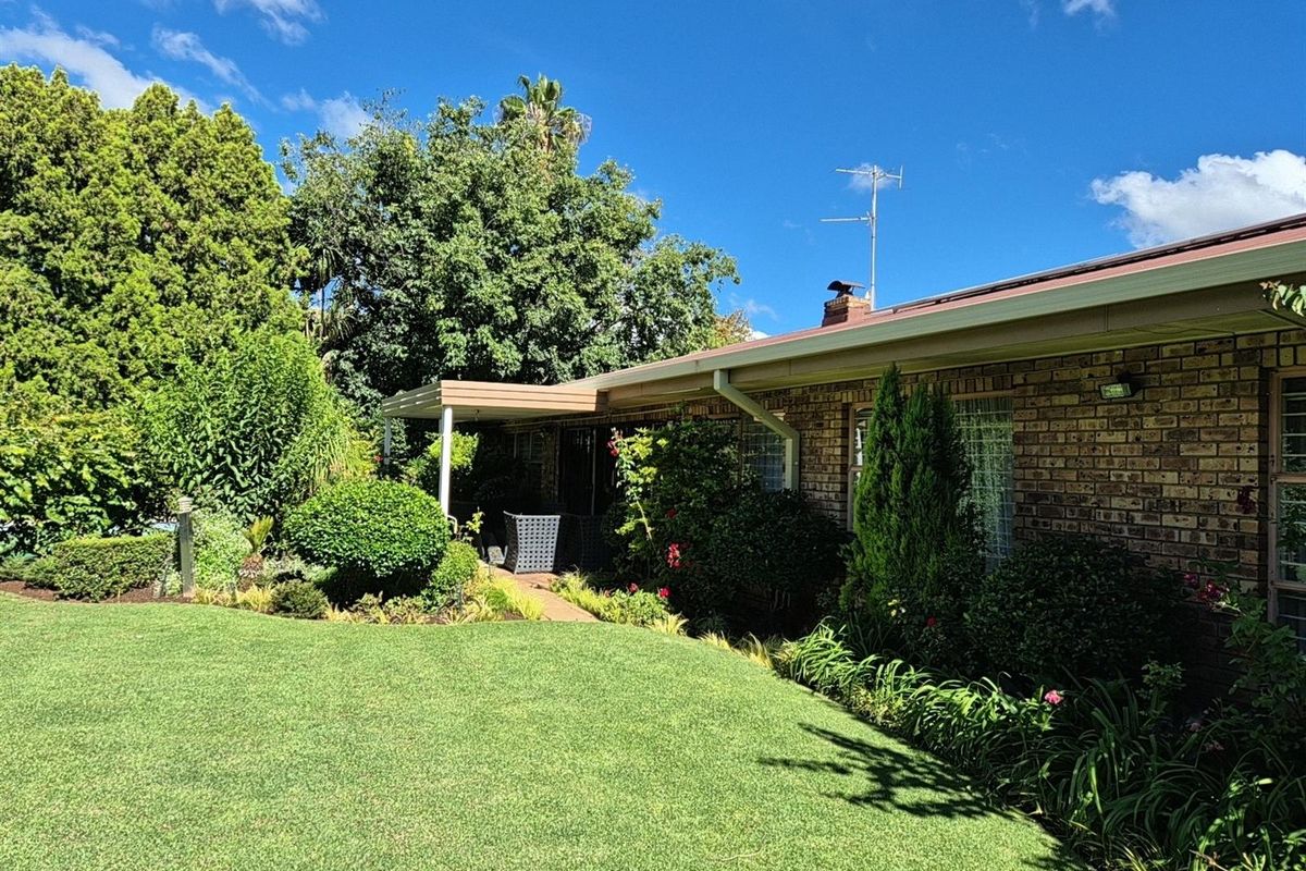 A well-maintained rear exterior view of the house featuring a brick facade, a covered patio area, and a lush, landscaped garden.