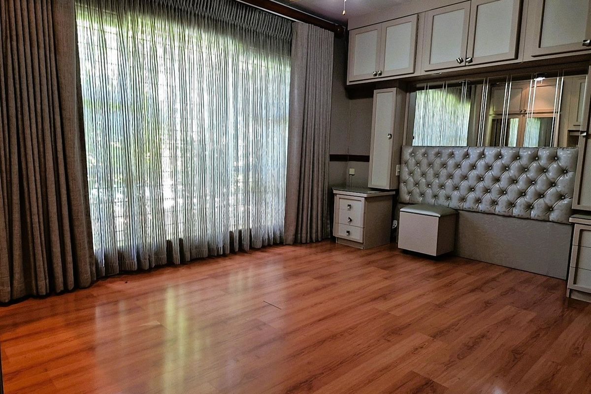 A bedroom featuring built-in cabinetry, a tufted headboard, laminate wood flooring, and floor-to-ceiling curtains providing access to the exterior.