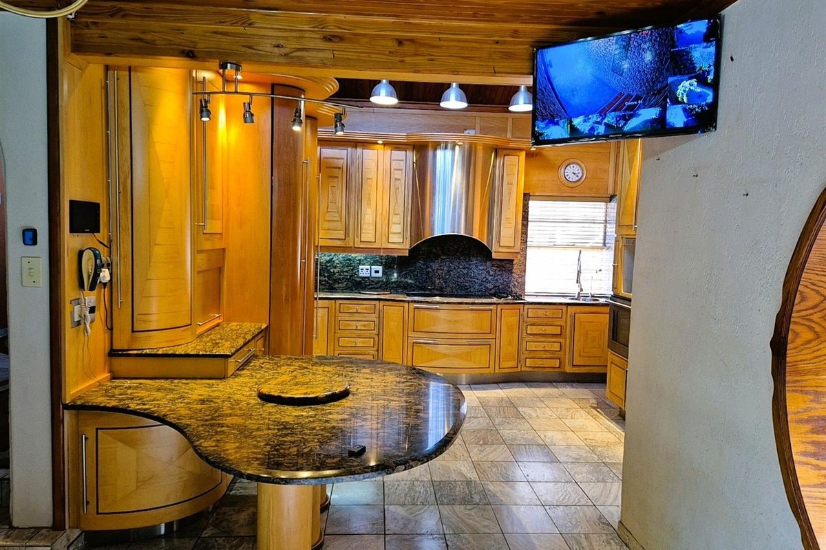 A spacious kitchen featuring warm timber cabinetry, granite countertops, a central breakfast bar, and a stainless steel extractor hood.