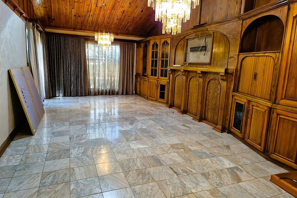 Spacious living area featuring high vaulted timber ceilings, polished marble-style floor tiles, and extensive built-in wooden cabinetry with integrated display shelving.