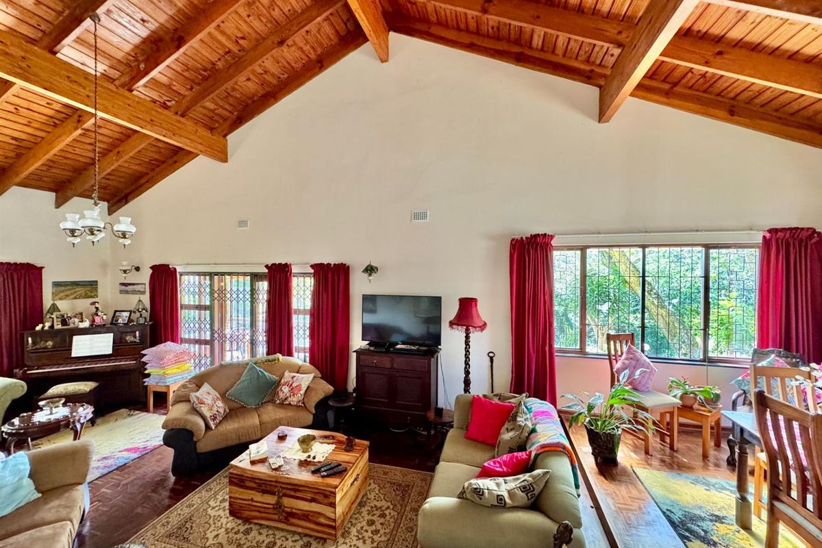 Spacious living area featuring high vaulted timber ceilings with exposed beams, large windows with security bars, and polished wooden flooring.