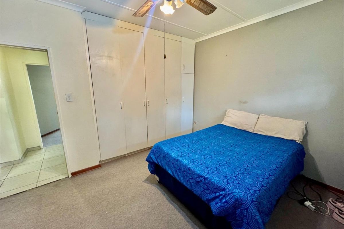 A bedroom featuring built-in cupboards, carpeted flooring, and a ceiling fan, providing a functional and comfortable living space.