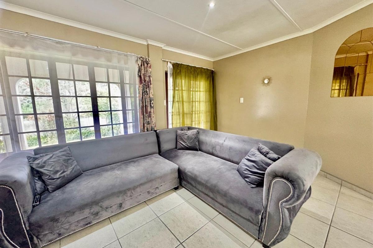 A living room featuring tiled flooring, large windows with natural light, and a neutral wall finish.