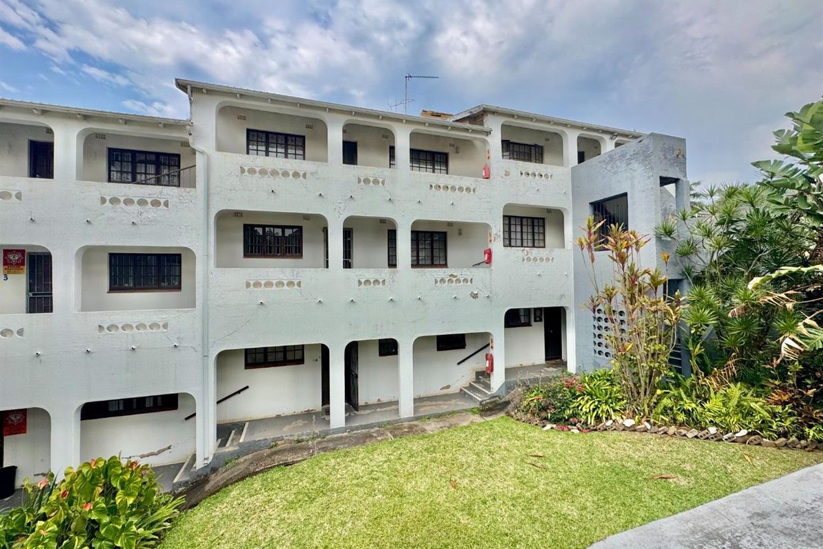 Exterior view of a multi-story apartment building featuring arched balconies, dark-framed windows, and a landscaped garden area at the base.