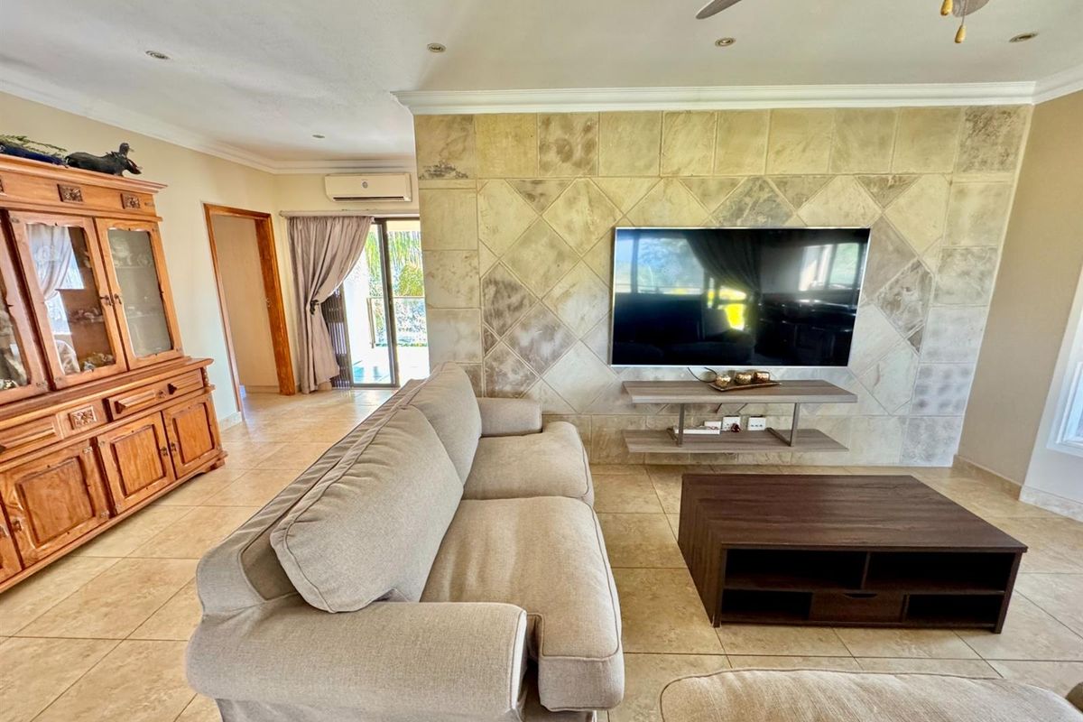 A comfortable living room featuring a distinctive stone-tiled feature wall, tiled flooring, recessed ceiling lighting, and a wall-mounted air conditioning unit.