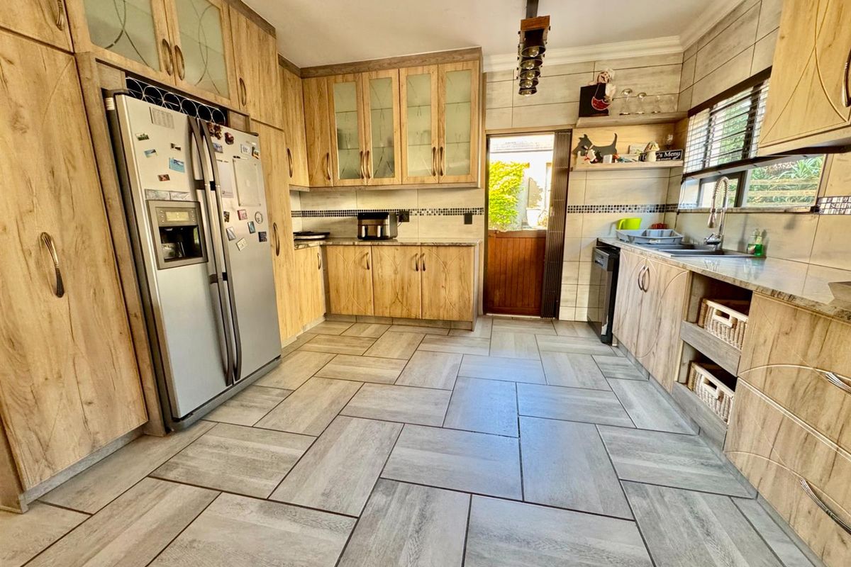 A well-maintained kitchen featuring wood-look cabinetry, tiled flooring, a double-door refrigerator, and a door leading to the exterior.