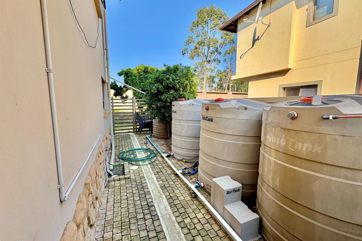 Side exterior area featuring multiple large water storage tanks with connected plumbing infrastructure and paved walkway.