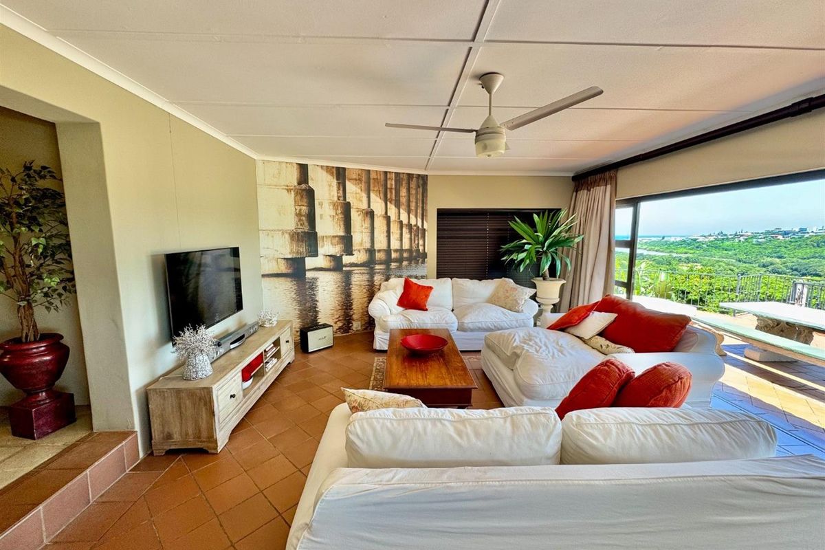 Spacious living room featuring terracotta floor tiles, a ceiling fan, and large sliding doors opening to an outdoor patio with scenic views.