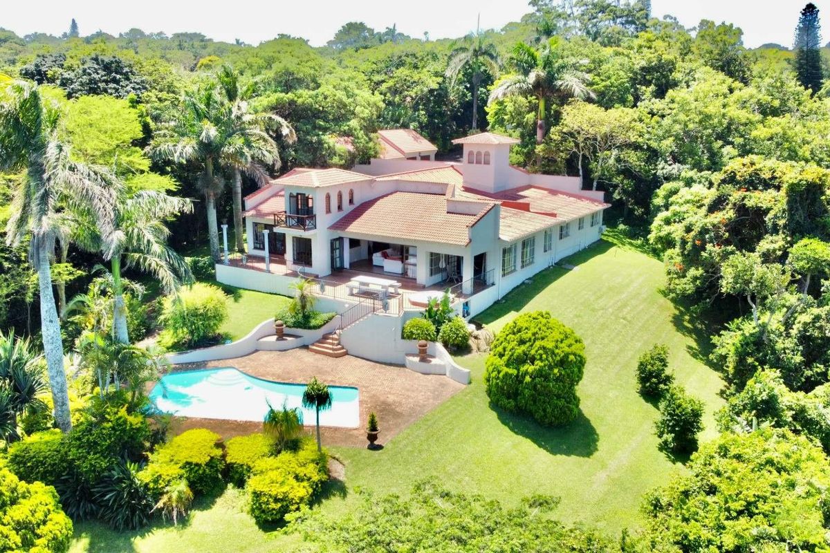 Aerial view of a spacious residential property featuring a large swimming pool, expansive landscaped garden, and a multi-level house with a tiled roof.
