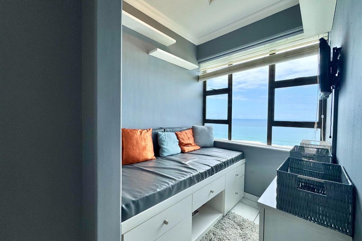 A compact bedroom featuring a built-in storage bench with integrated drawers, large windows offering ocean views, and modern crown molding.