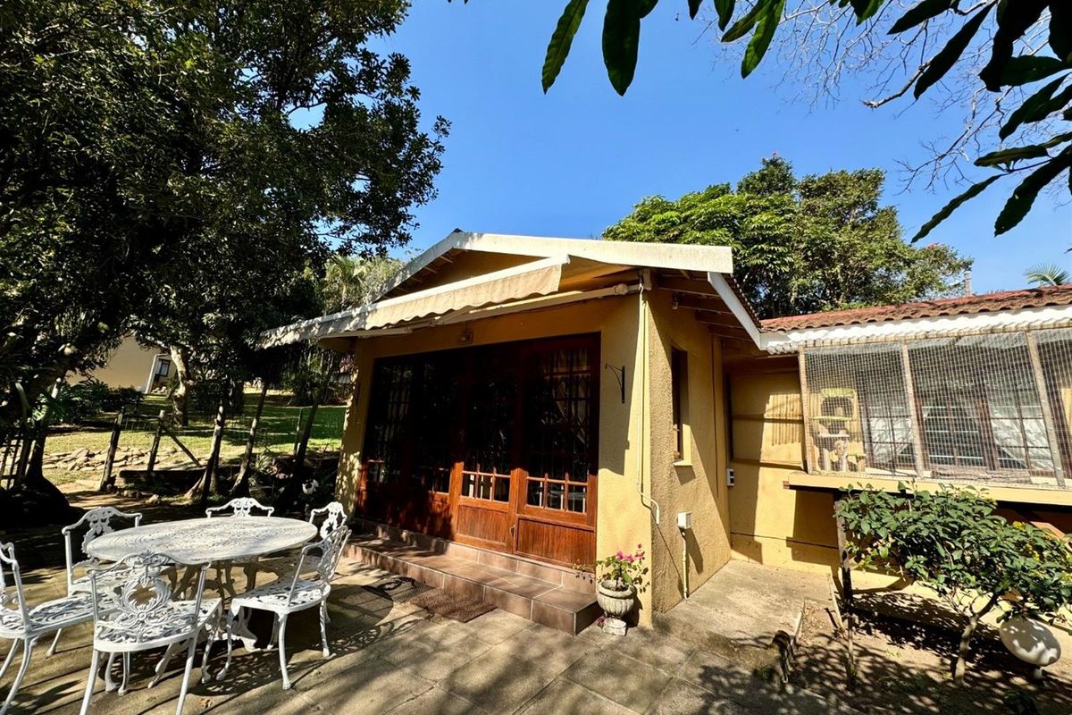 A rear exterior view of the property featuring a paved patio area, timber-framed glass doors, and a retractable awning.