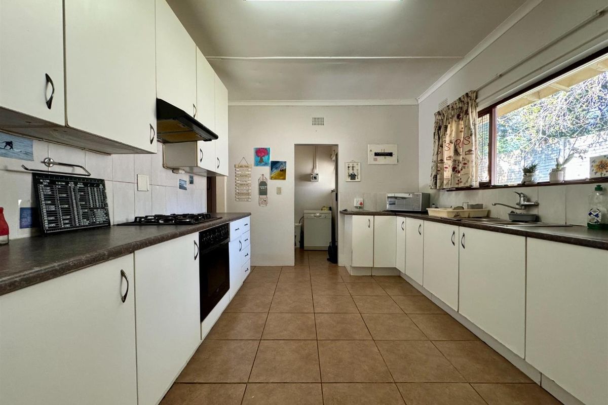A functional kitchen featuring white cabinetry, dark laminate countertops, a gas hob, built-in oven, and tiled flooring, with an adjacent utility area.