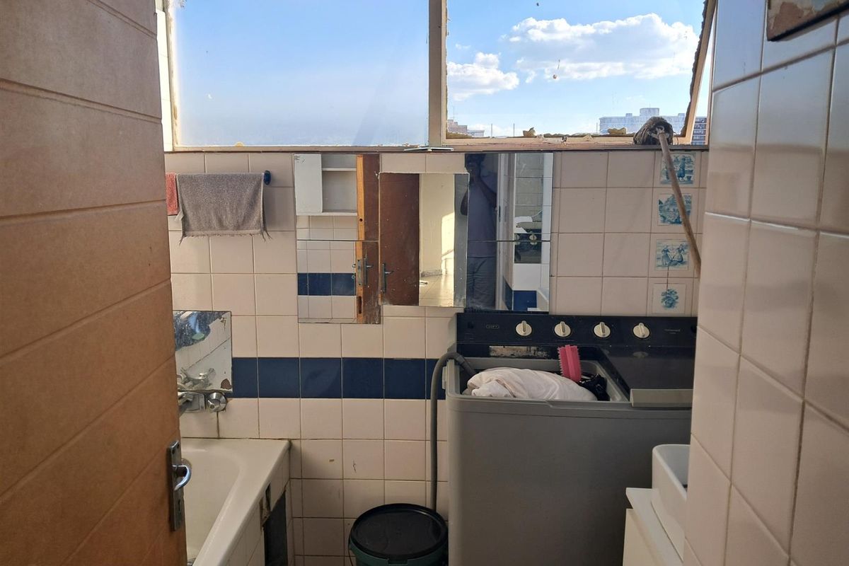 A dated bathroom featuring wall-to-wall tiling, a built-in bathtub, and a laundry area. The space requires significant maintenance and renovation.