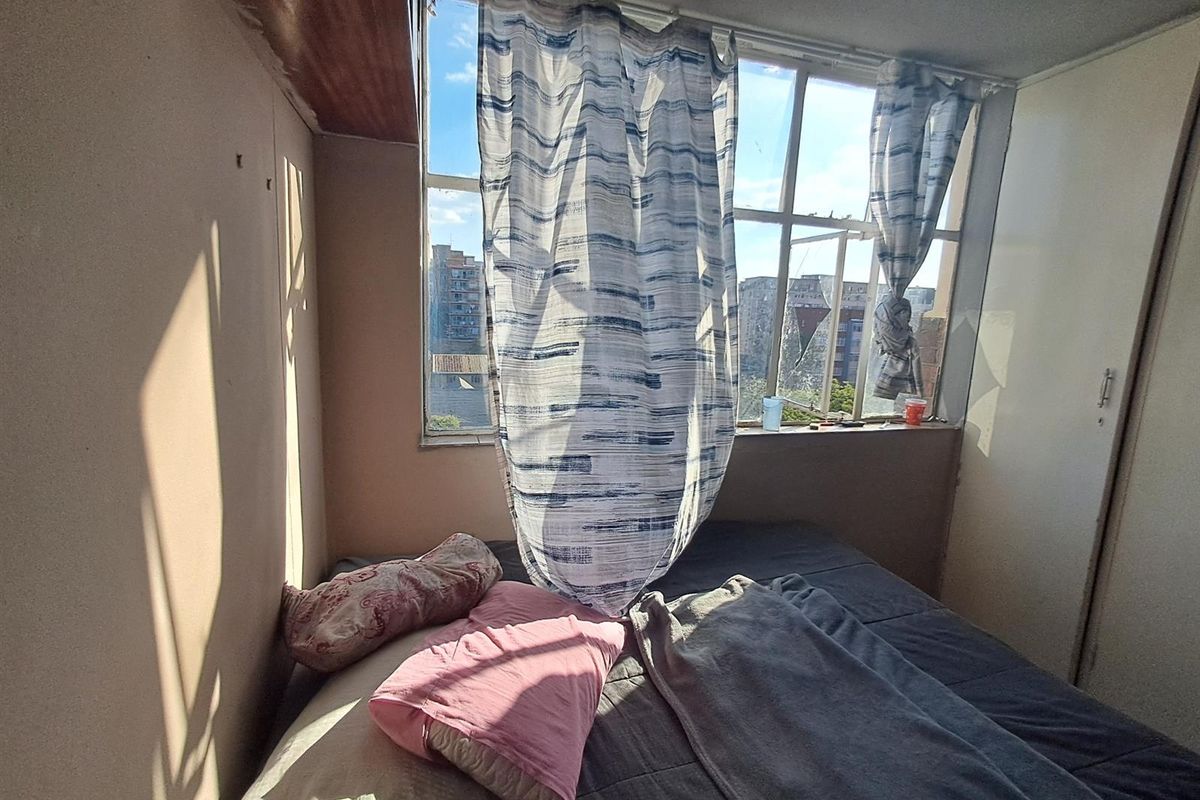 A bedroom featuring a large window with natural light, built-in cupboard, and basic finishes in need of cosmetic updates.