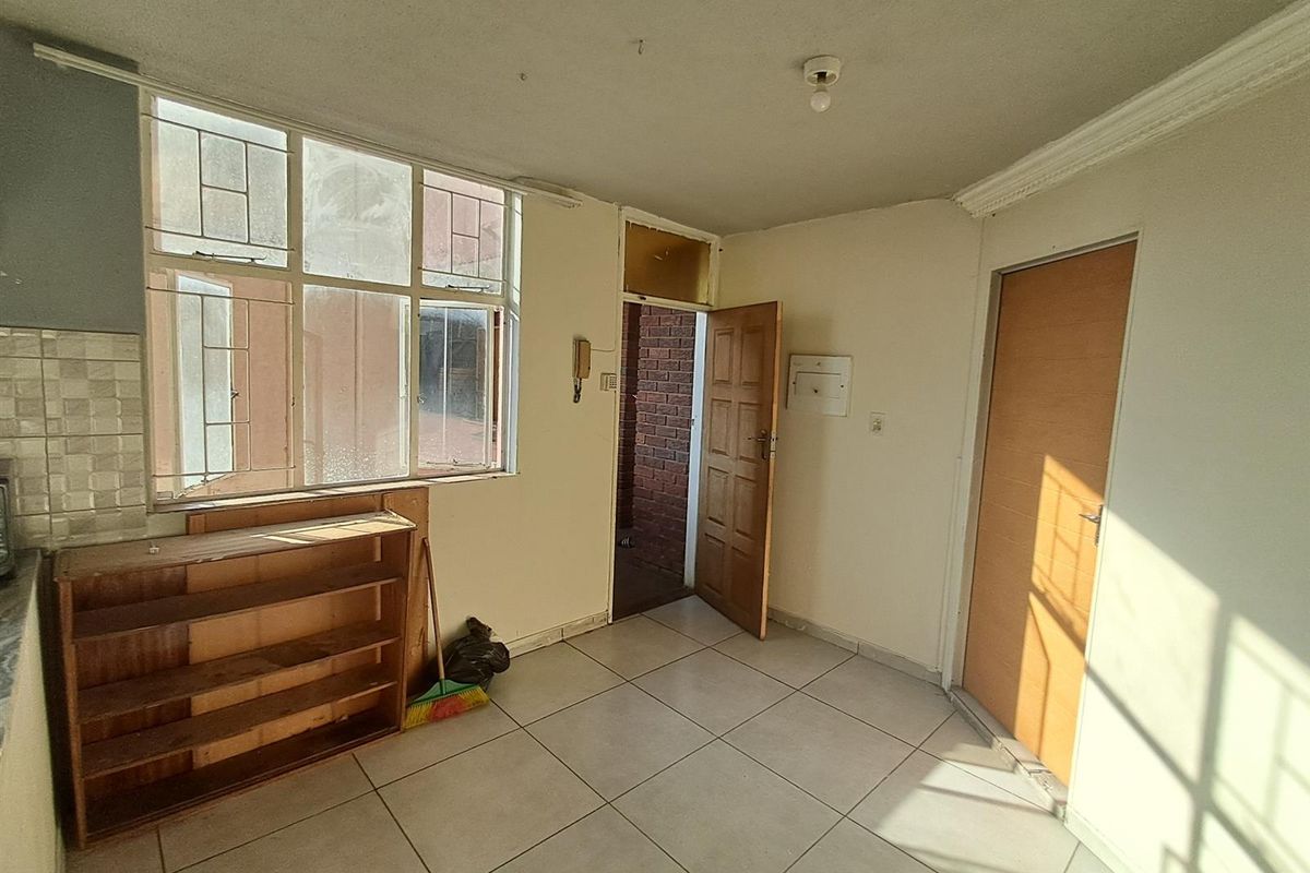 A dated interior space featuring tiled flooring, large windows, and multiple wooden doors, requiring cosmetic updates to modernize the finishes.