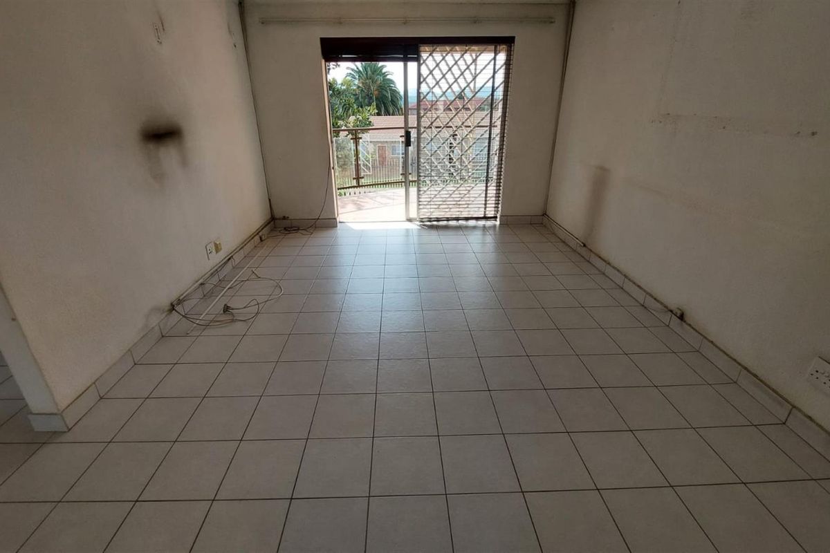 An empty living room featuring ceramic floor tiles and a sliding glass door with a security gate leading to an outdoor area.