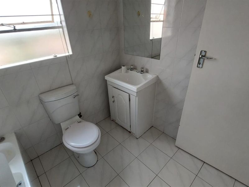 A functional bathroom featuring a bathtub, toilet, and vanity basin with tiled walls and flooring, offering a clean, neutral base for potential updates.