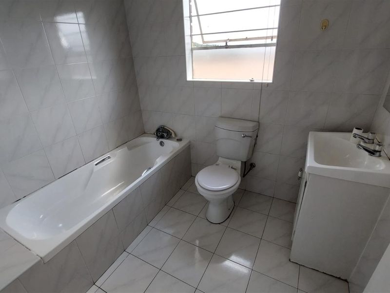 A clean, functional bathroom featuring a built-in bathtub, toilet, and vanity basin with neutral wall and floor tiling.