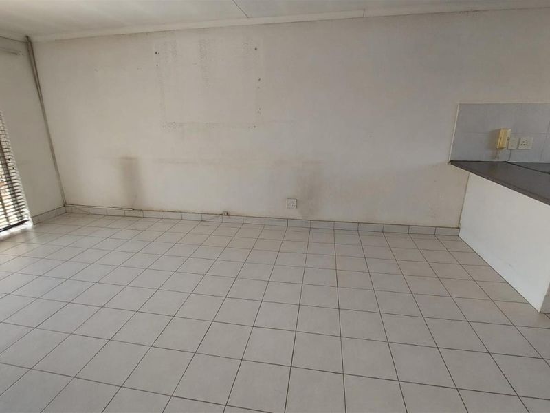 An empty open-plan living and kitchen area featuring tiled flooring, a built-in kitchen counter with stove, and large windows with blinds.