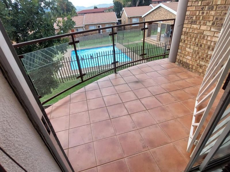 A private balcony featuring tiled flooring and a modern glass balustrade, offering a clear view of the complex pool area below.