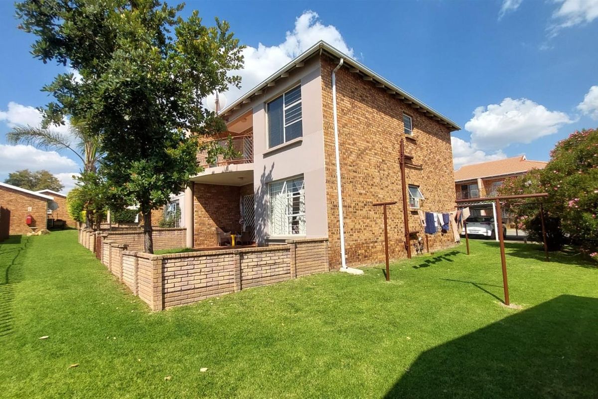 Rear view of the townhouse featuring a brick facade, a private balcony, and a surrounding garden area with a brick boundary wall.