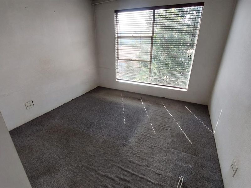 An empty bedroom featuring carpeted flooring, a large window with blinds, and neutral wall finishes, offering a blank canvas for personalization.