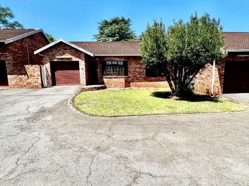 Front view of a face brick townhouse featuring a tiled roof, single garage, and a paved driveway with a small front lawn.