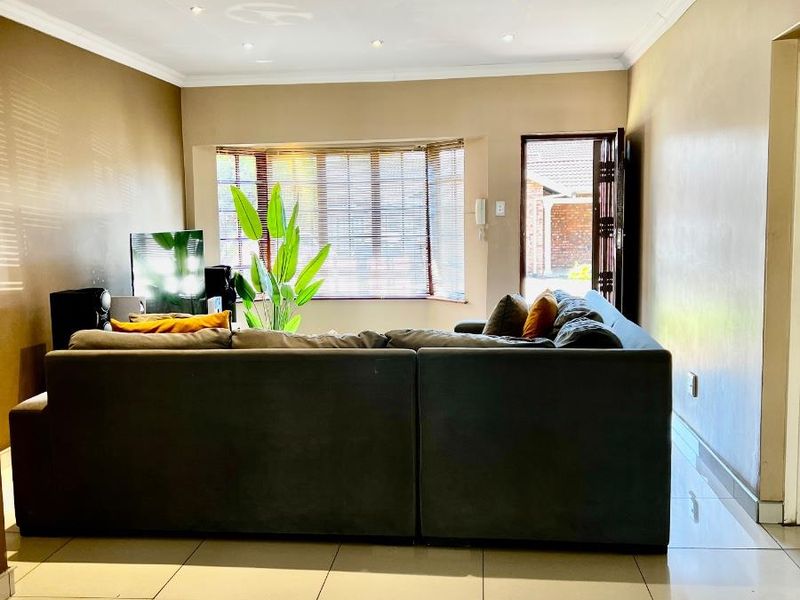 A well-lit living room featuring large format floor tiles, recessed downlighting, and a bay window with fitted blinds.