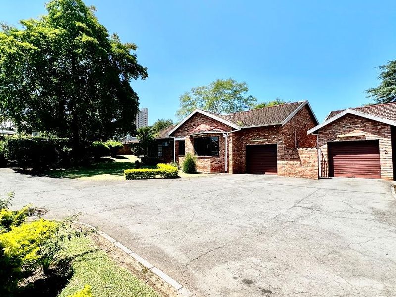 Front exterior view of a brick townhouse featuring a double garage, paved driveway, and established garden surroundings.