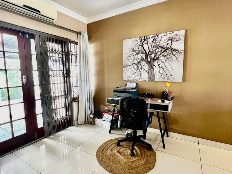 A bright home office featuring tiled flooring, split-system air conditioning, and double doors providing access to the outdoor area.