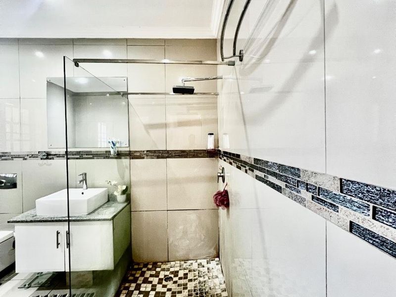 Modern bathroom featuring a glass-enclosed walk-in shower, wall-mounted vanity with vessel sink, and decorative mosaic tile accents.