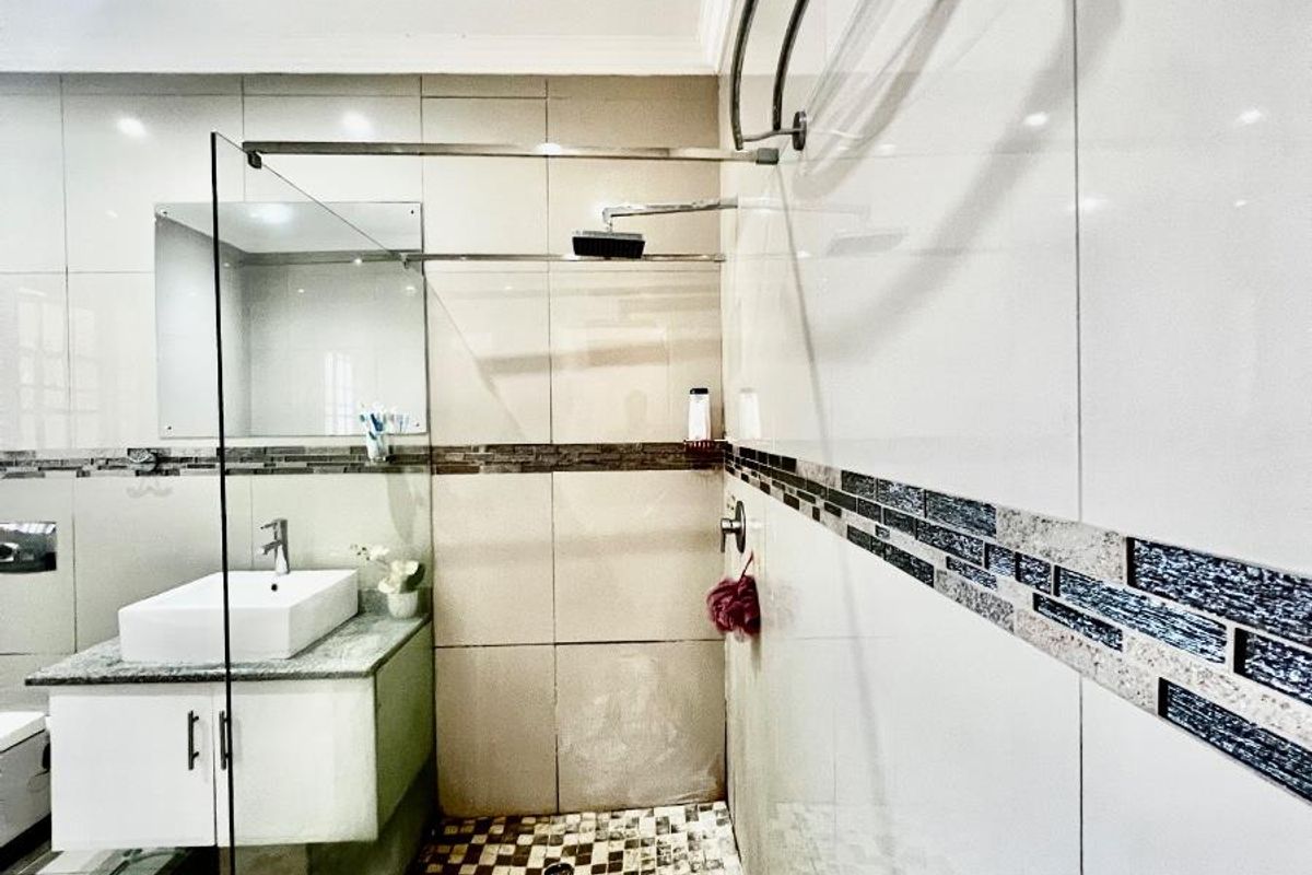 Modern bathroom featuring a glass-enclosed walk-in shower, wall-mounted vanity with vessel sink, and decorative mosaic tile accents.