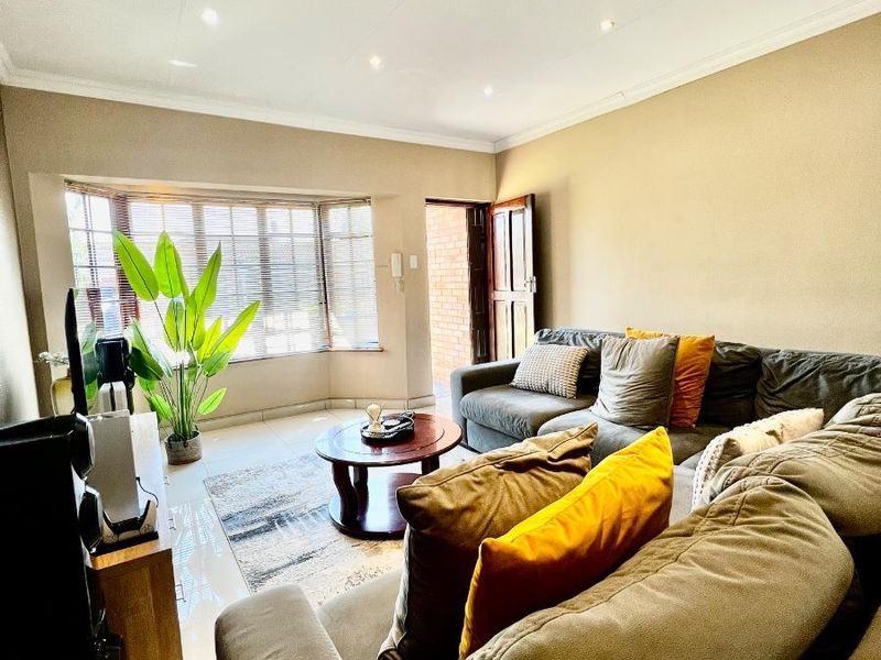 A comfortable living room featuring a large bay window, tiled flooring, and recessed downlighting, creating a bright and inviting space.